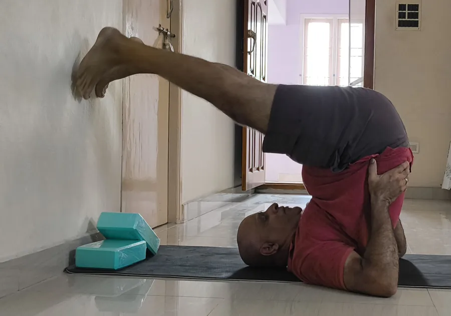 Suresh on a mat with his legs over his head and a block under his feet